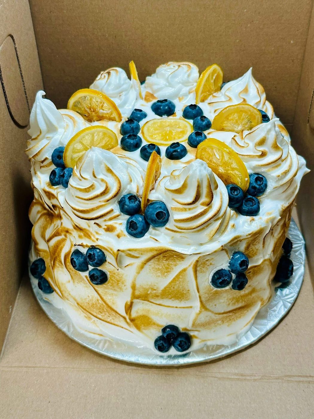 Lemon meringue cake torched golden and topped with blueberries and lemon