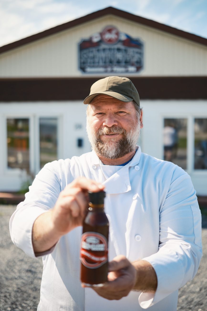 Rob holding a bottle of house-made sauce outside the shop